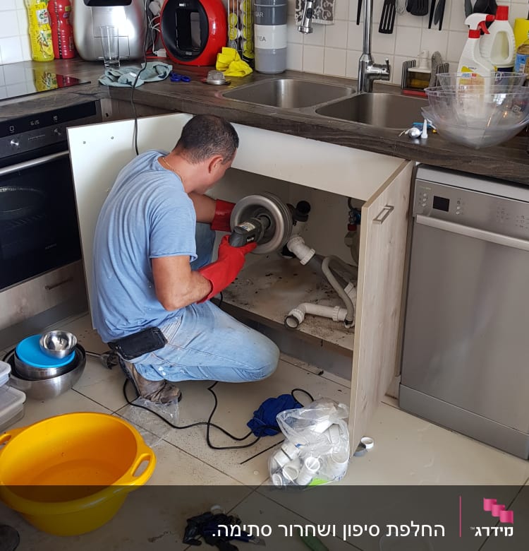 אדם מתקן צנרת מתחת לכיור במטבח